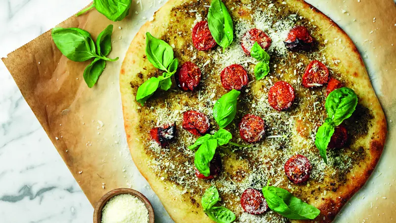 Nybakad pizza med pesto och tomater bakad på färsk pizzadeg